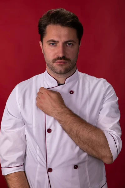 Cansado unshaven guapo chef toma off uniforme después de largo turno en rojo telón de fondo —  Fotos de Stock