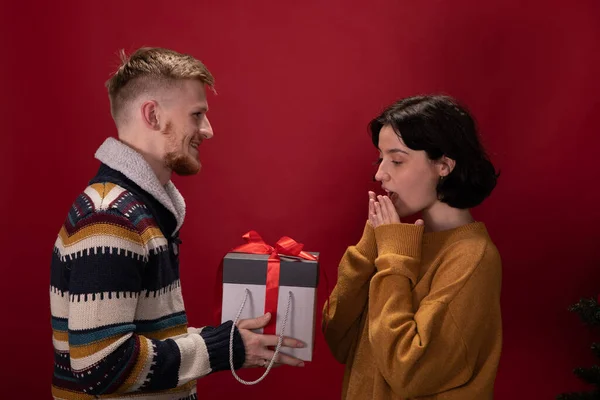 young handsome red bearded man gives his surprised girlfriend Christmas present