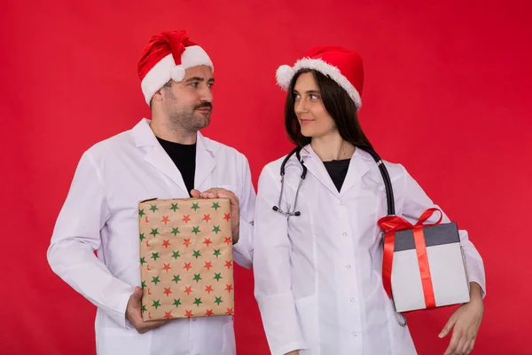 Два врача в шляпах Санта-Клауса держат рождественские подарочные коробки глядя друг на друга — стоковое фото