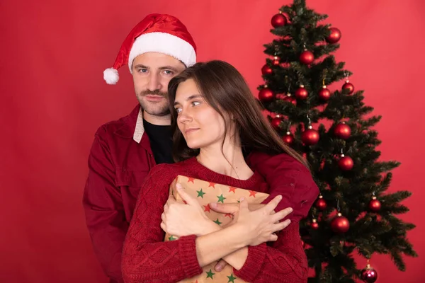 Pareja de amantes con el regalo se abraza suavemente en el fondo del árbol de Navidad — Foto de Stock