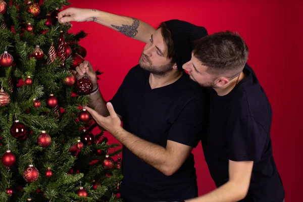 Joven gay macho pareja colgando decoraciones en navidad árbol juntos — Foto de Stock