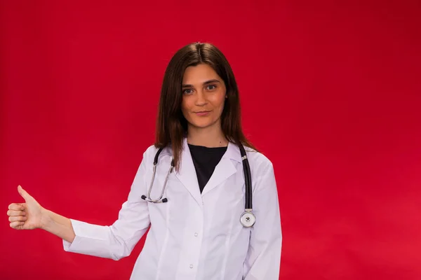 Aantrekkelijke langharige brunette vrouwelijke arts toont duim omhoog kijken naar camera — Stockfoto