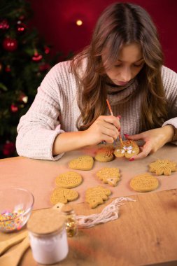 Uzun saçlı esmer bir kız Noel kurabiyelerini tek başına dekore ediyor.