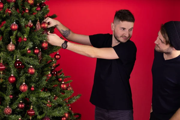 Joven sonriente pareja gay colgando decoraciones en árbol de Navidad juntos — Foto de Stock