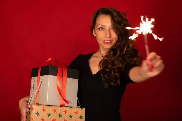 Mujer bonita con regalos navideños, bengala ardiente sobre fondo rojo, espacio para copiar — Foto de Stock