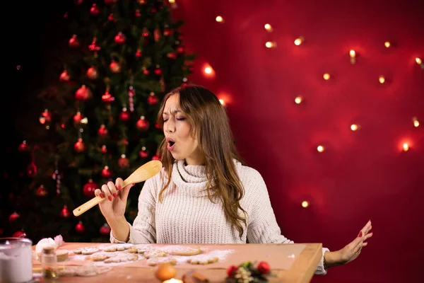 Mujer atractiva alegre cantando canciones de Navidad usando espátula de cocina — Foto de Stock