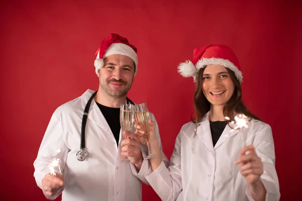 Två läkare i jultomten hattar hejar champagne flöjter och brinnande tomtebloss — Stockfoto