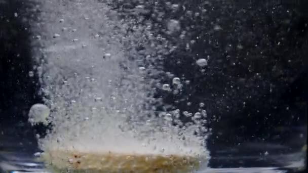 Macro shot de comprimido efervescente dissolve-se com bolhas em água, câmera lenta — Vídeo de Stock