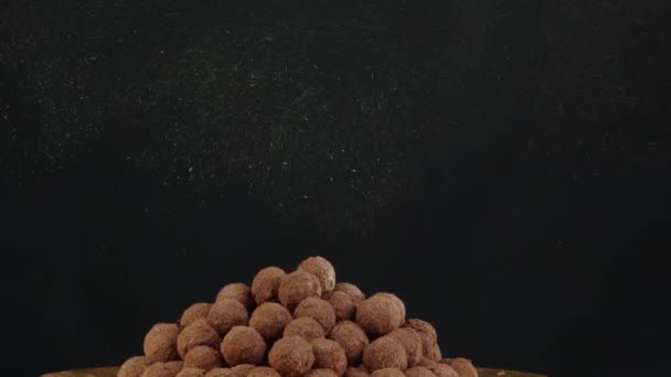 Zbliżenie złoto błyszczący pył wylewa się na stos trufli czekoladowych na czarnym tle — Wideo stockowe