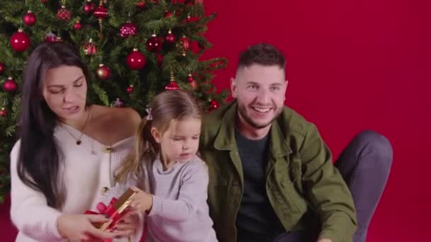 Familia feliz clasificación de regalos de Navidad cerca del árbol de Navidad en el fondo festivo rojo — Vídeo de stock