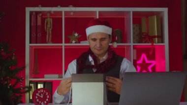 Noel Baba şapkalı 40 'lı işadamı Noel süslemeli ofiste sihirli hediye kutusunu açıyor