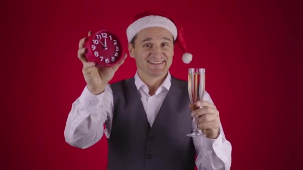 산타 모자를 쓴 쾌활 한 사람이 새해가 되기 몇 초 전에 시계를 잡고 샴페인을 마신다 — 비디오