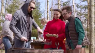 Arkadaşlar yaz pikniğinde barbekü yapar yakışıklı adam tabağa ızgara et koyar.