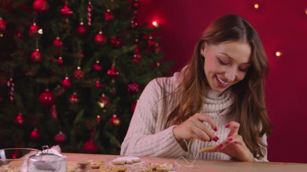 Cute smiling brunette young woman hung Christmas gingerbread on linen string — Stock Video