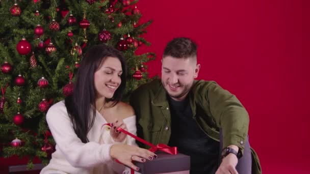 Young loving couple opening long awaited new year gift sitting near xmas tree — Stock Video