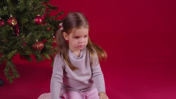 Little cute girl unpacks Christmas gift sitting near xmas tree, New Years Eve — Stock Video