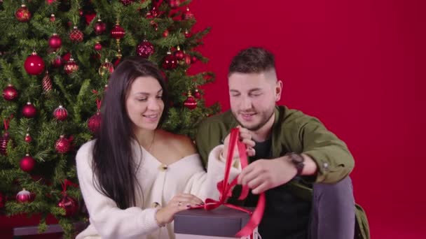 Young loving couple opening long awaited new year gift sitting near xmas tree — Stock Video