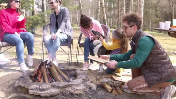 Szczęśliwi przyjaciele o grill party w przyrodzie, młody człowiek dodaje drewna do ognia — Wideo stockowe