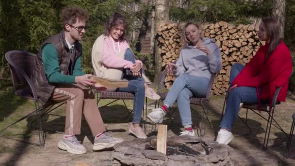 Grupa ludzi cieszących się kempingiem na świeżym powietrzu, szczęśliwi przyjaciele siedzi wokół ogniska — Wideo stockowe