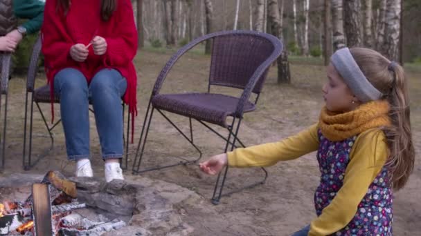 Little cute girl odgrywa w pobliżu ogniska na pikniku i frytki żywności na drewnianym kiju — Wideo stockowe