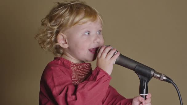 Милая маленькая девочка поет песню в микрофон, забавный малыш наслаждается вещанием — стоковое видео