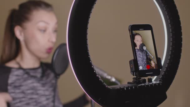 매력적 인 여성이 스마트폰과 마이크를 사용하여 온라인 발성 강의를 기록 한다 — 비디오