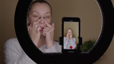 Pozitif kadın vlogger burun bölgesi üzerinde yüz kaldırma egzersizleri yapıyor, blog yazıyor