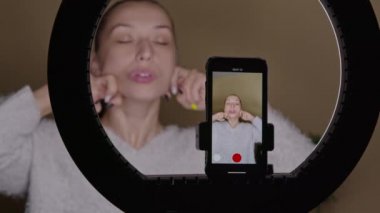Genç kadın vlogger yüz hatları için online cilt kaldırma egzersizleri yapıyor.