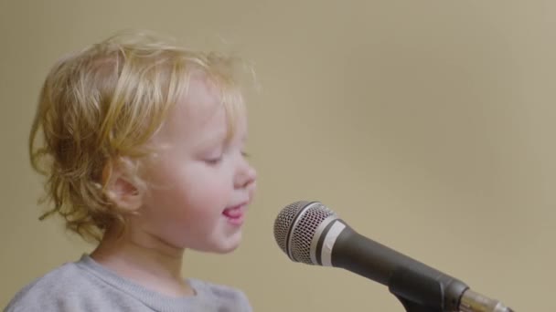 Милая маленькая девочка поет песню в микрофон, забавный малыш наслаждается вещанием — стоковое видео