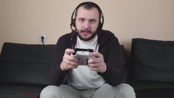 Souriant beau gamer masculin avec casque jouer jeu vidéo en ligne tenant joystick — Video