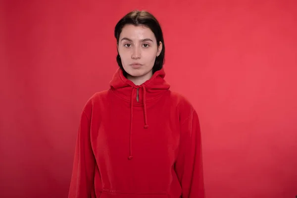 Menina morena com capuz vermelho olhando para os lábios de pato da câmera no fundo do estúdio vermelho — Fotografia de Stock