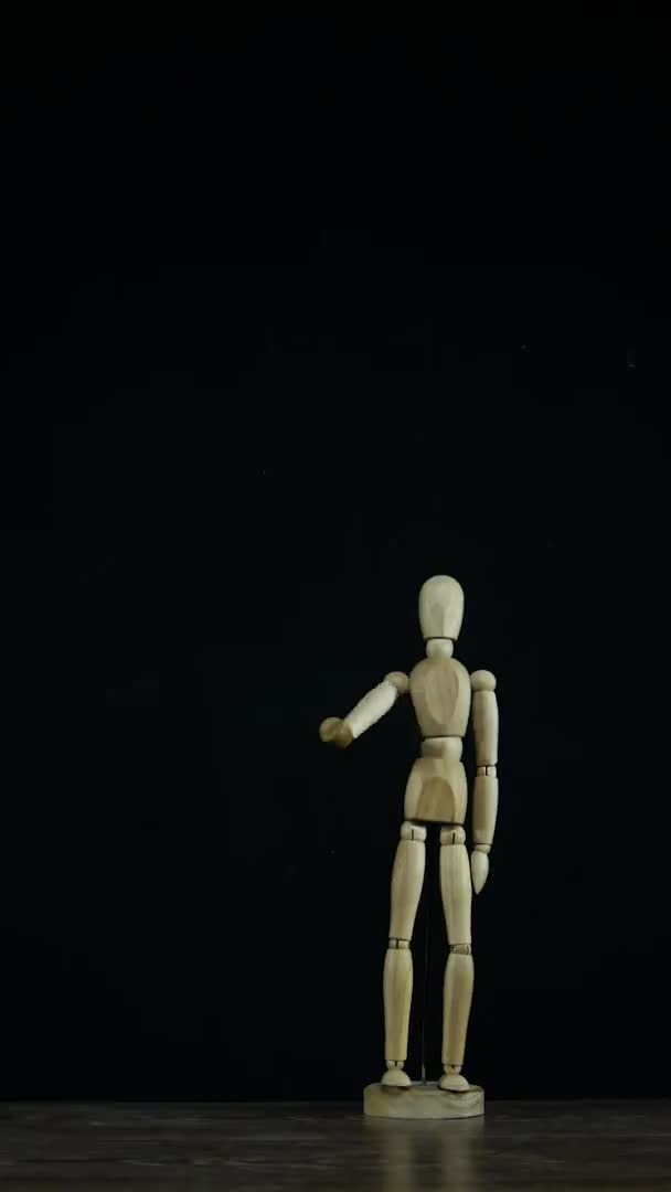 Вертикальне відео Зупинка дерев'яна фігура манекен махає рукою в студії на чорному тлі, показуючи прощання — стокове відео