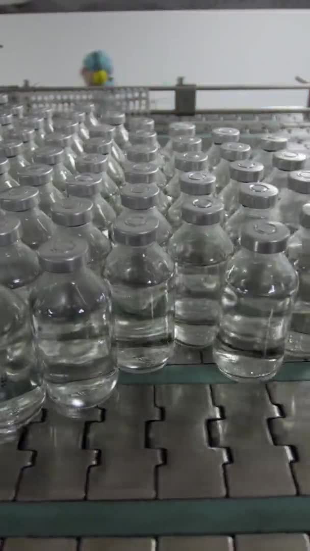 Вертикальное видео стеклянные бутылки заполнены и запечатаны резиновыми и алюминиевыми колпачками на транспортерной линии медицинского решения — стоковое видео