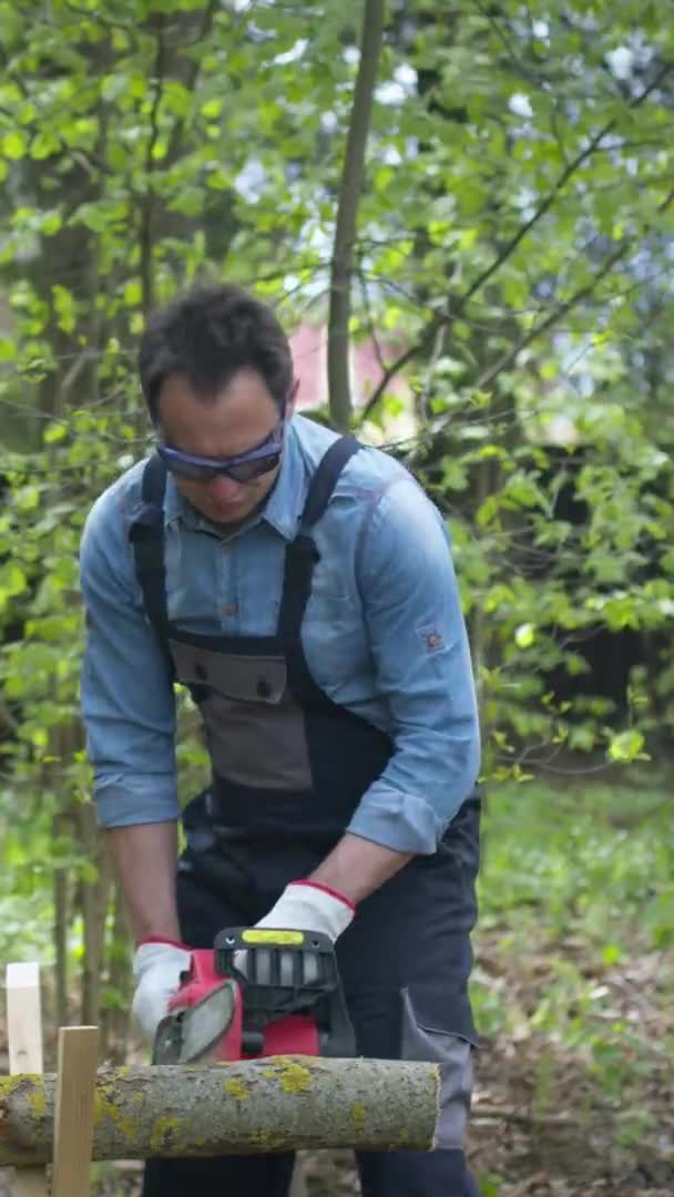 Vertikaler Schuss Schöner Holzfäller in Arbeitsuniform sägt Holz mit Kettensäge auf Sägepferd — Stockvideo