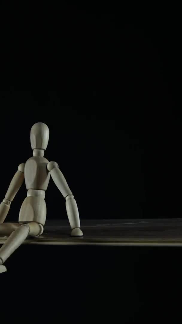 Vertical video Stopmotion figura de madera maniquí procrastina en estudio sobre fondo negro sentado y agitando las piernas para títulos — Vídeo de stock