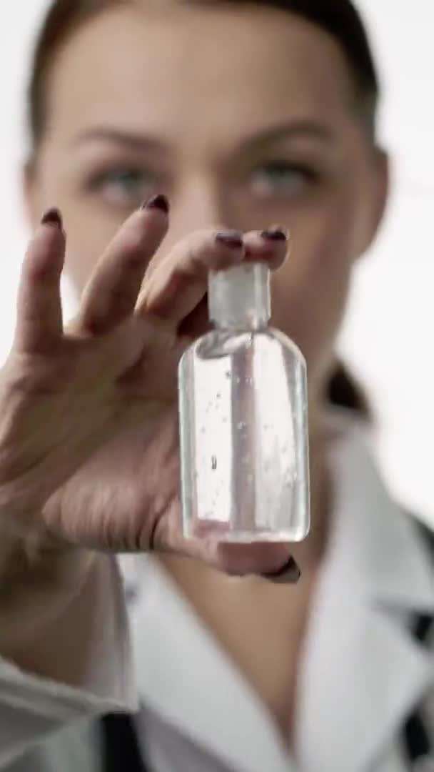 Tiro vertical médico fêmea bonita mostra pequena garrafa de mão antibacteriana anti-séptico — Vídeo de Stock