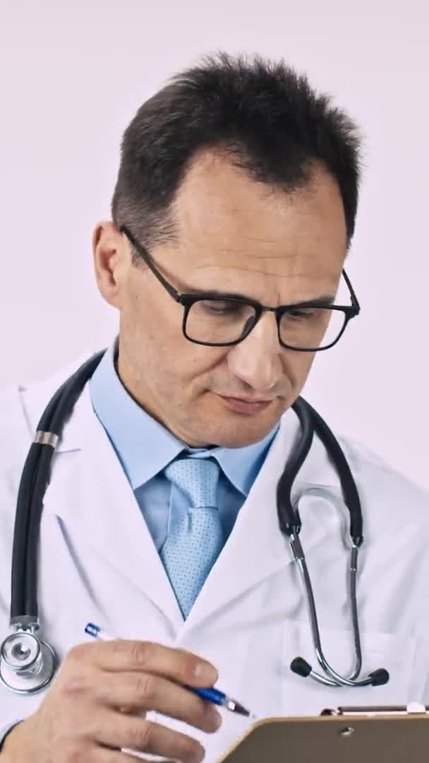 Dikey çekim yakışıklı doktor reçeteyi panoya yazar gülümseyerek kameraya bakar — Stok video