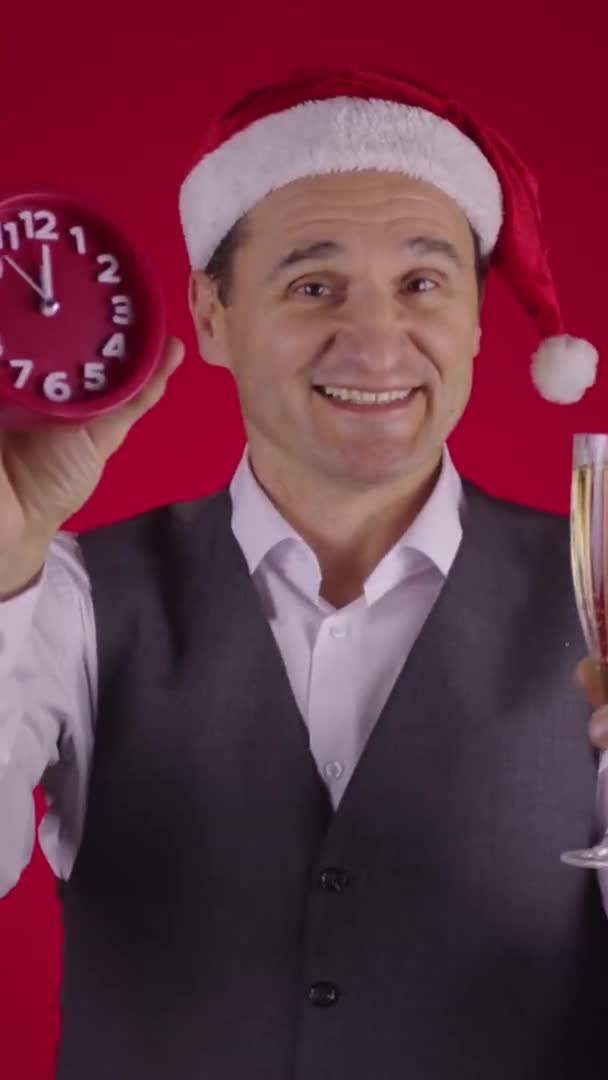 Senkrecht erschossen Fröhlicher Mann mit Weihnachtsmütze hält Uhr, die Sekunden vor Neujahr Champagner trinkt — Stockvideo