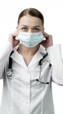 Dikey çekim. Tıp üniformalı güzel laboratuvar teknisyeni koruyucu maske takmış.