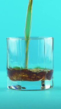 Dikey video 4K yakın plan, Stüdyoda mavi arka planlı, düşük bardakta duran gazlı kola soğuk içecek.