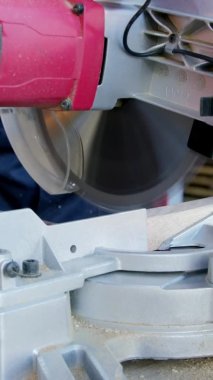 Dikey çekim yapan koruyucu eldivenli marangoz Mitre Testeresi 'ndeki ahşap meşe barını kesiyor.