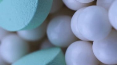 Dikey video yuvarlak yeşil ilaçlar dağınık küçük beyaz granüller üzerinde yatar. Kapatma döndürmesi
