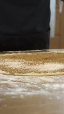 Dikey çekim yakın fırıncı hamur hamurundan rulo yapar şeker ve tarçın ile hamur serpiştirir