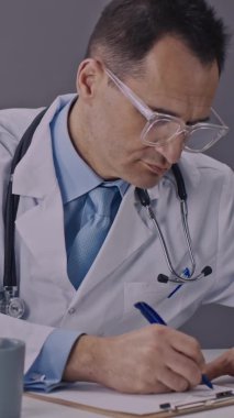 Dikey çekim odaklı doktor pano ile çalışır tıbbi kayıtları yazar masaya yorgun yatar