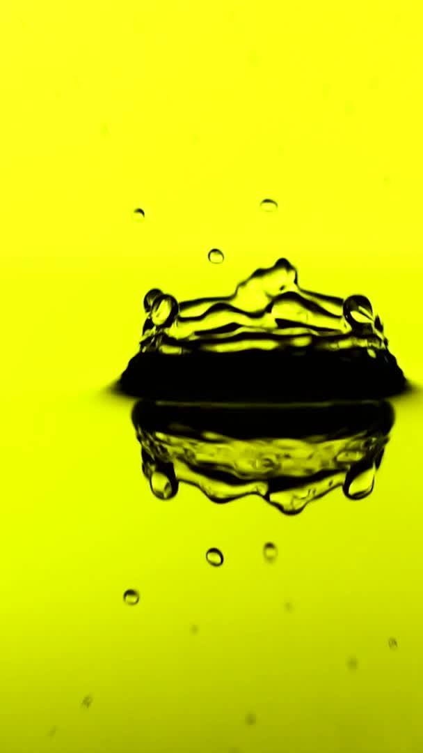 Vídeo vertical Uma gota de água cai sobre a superfície de um óleo em câmera lenta. Fundo amarelo. — Vídeo de Stock