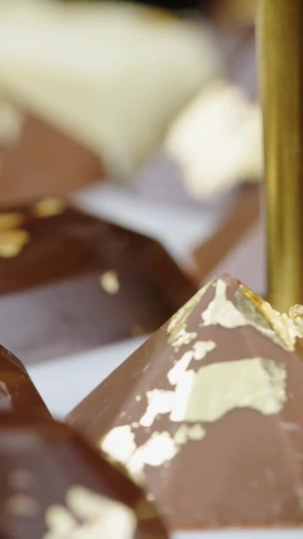 Vidéo verticale Gros plan ensemble de bonbons au chocolat premium avec décoration en feuille d'or tournant — Video