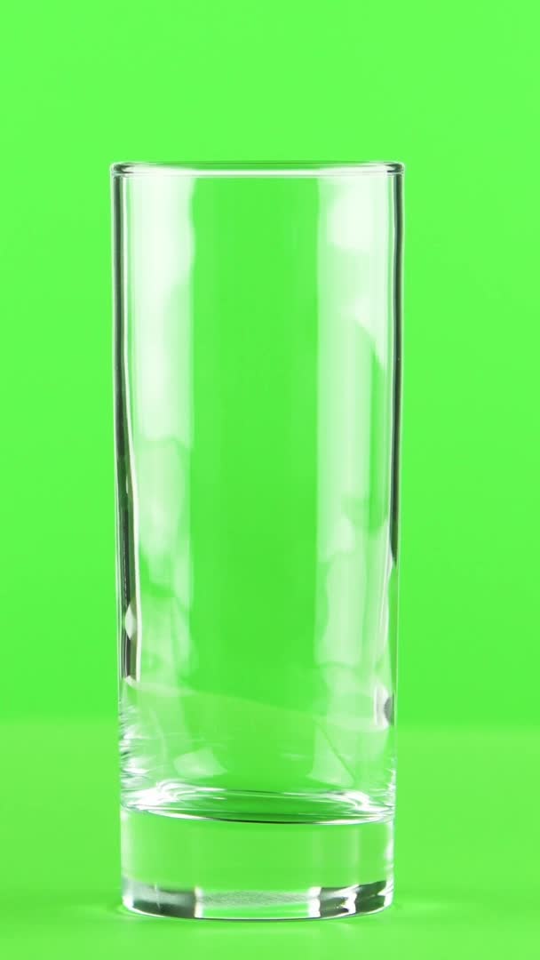 Вертикальное видео Сок заливки в стекло изолированы на светло-зеленом фоне — стоковое видео