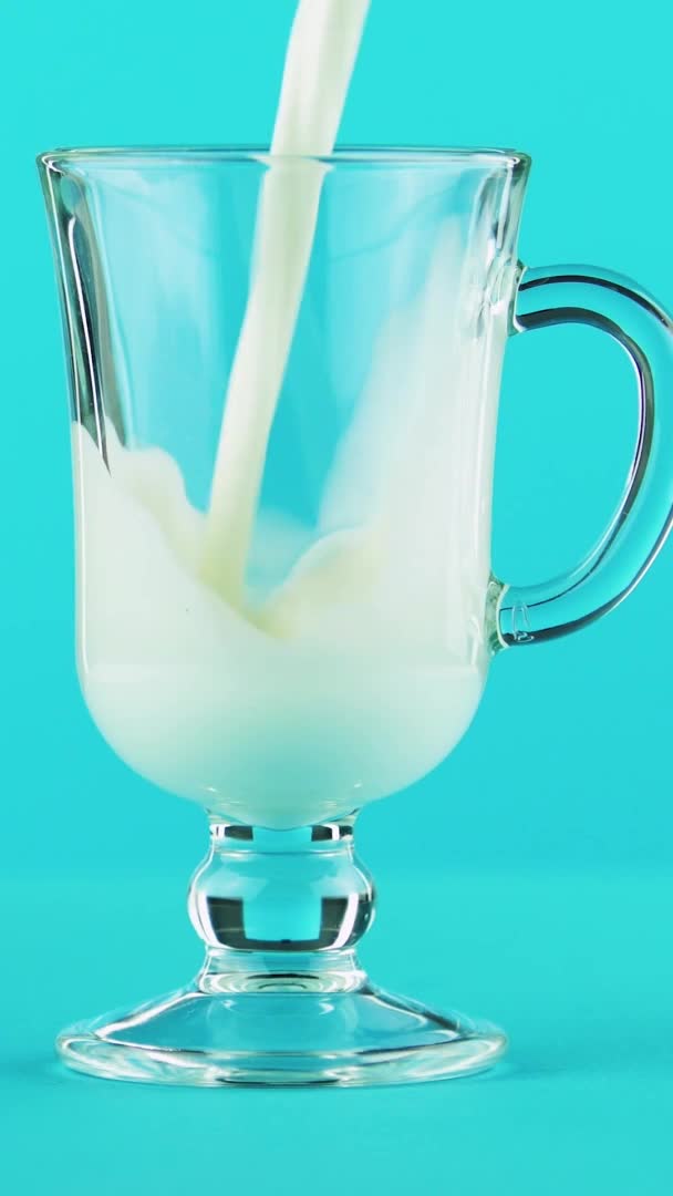 Vídeo vertical 4K close-up de leite bebida fria bebida pooring em latte caneca de vidro fundo azul no estúdio — Vídeo de Stock
