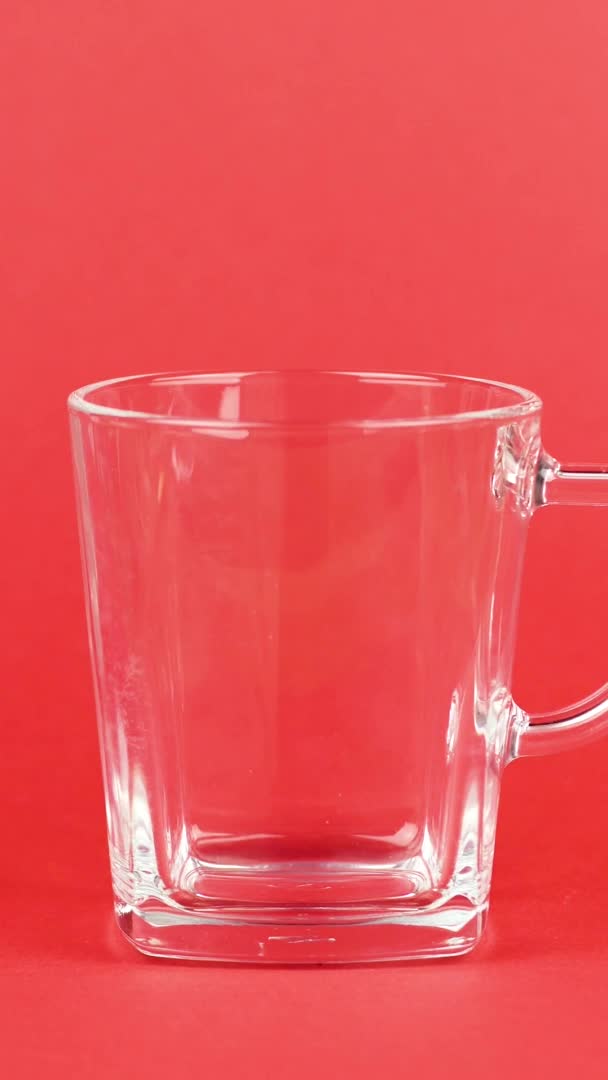 Video verticale I chicchi di caffè volano rapidamente, tazza di vetro trasparente, sfondo rosso. Concetto mattina — Video Stock