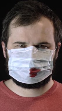 Tıbbi maskeli, kanlı, dikey, hasta bir adam yeni bir maske takıyor. Covid-19 konsepti